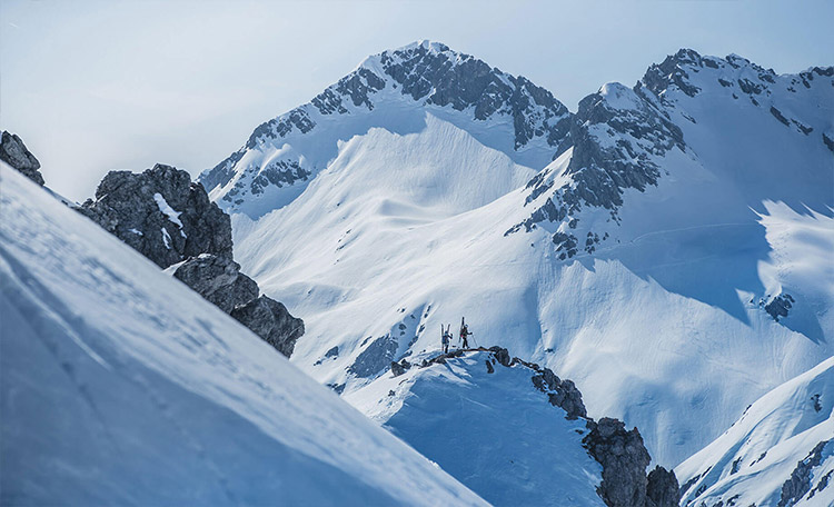 Bij het freeriden kun je kiezen: een korte hike vanaf het bergstation of toch de eenzame skitocht buiten de skigebieden. Twee freeriders lopen op met sneeuw bedekte bergen.