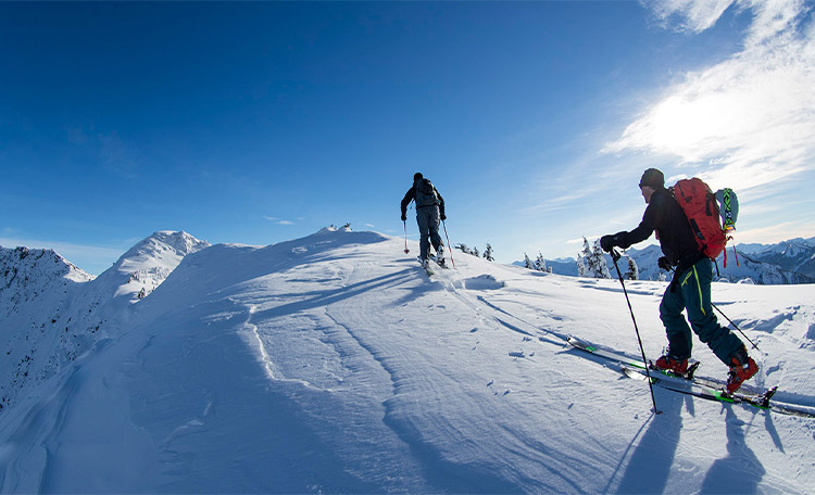 Twee toerskiërs beklimmen in de zon een besneeuwde berg.