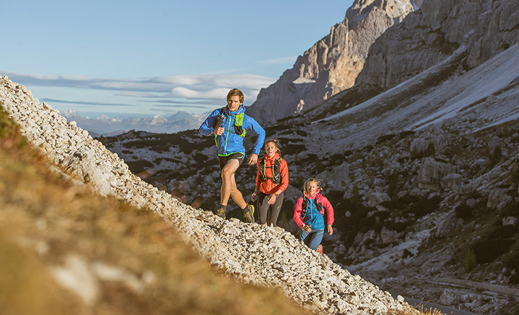 Drie trailrunners rennen in de zon een berg op.